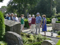 Eine Gruppe von Menschen steht auf dem Friedhof und betrachtet einen Grabstein. Eine Gruppe von Menschen steht auf dem Friedhof.