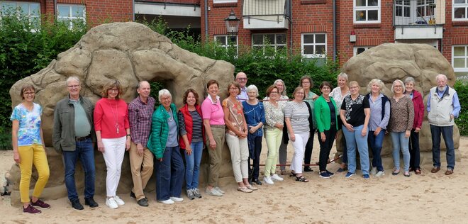 Mehrere Frauen und Männer stehen nebeneinander vor Klettersteinen im Sand. Mehrere Frauen und Männer stehen nebeneinander.