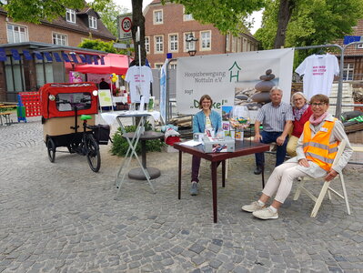Vier aktive Hospizler sitzen am Stand, der für das Fest für Demokratie und Frieden entstand. Im Hintergrund steht die Rikscha. Vier aktive Hospizler sitzen am Stand, der für das Fest für Demokratie und Frieden entstand. Im Hintergrund steht die Rikscha.