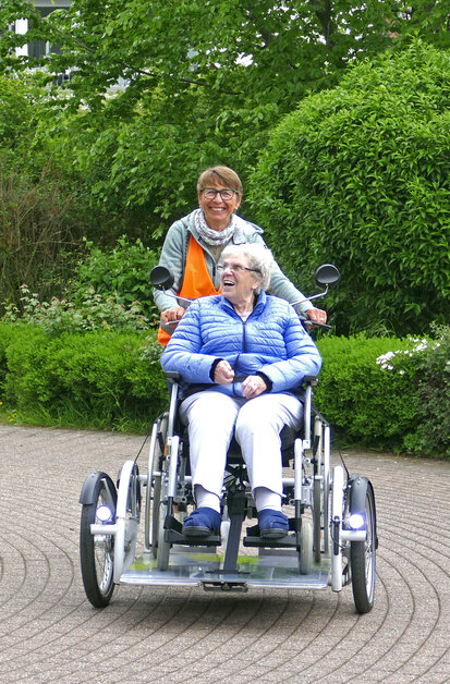 Eine im Rollstuhl sitzende Frau, wird auf einem Fahrrad gefahren.  