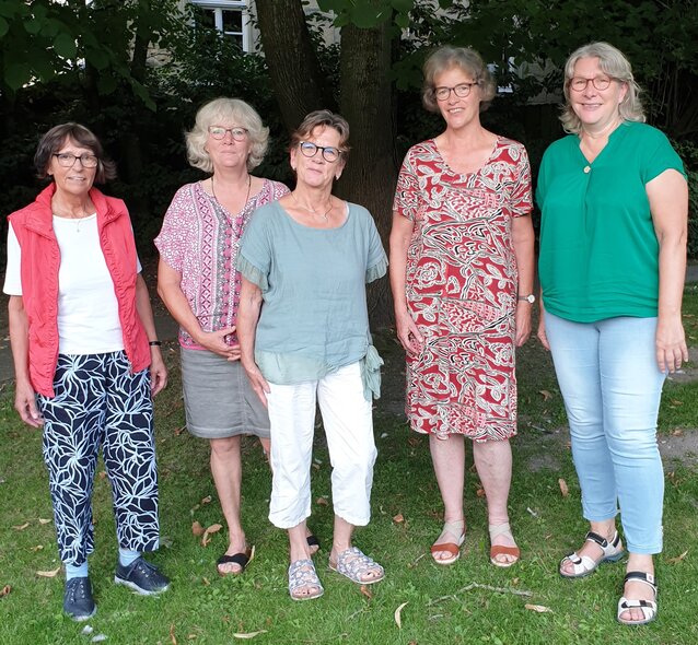 Das Bild zeigt ein Foto von fünf der acht Trauerbegleiterinnen stehend vor einem Busch Das Team des Trauerecafés
