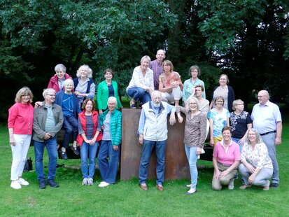 Das Foto zeigt eine Gruppe Sterbebegleiterinnen und Sterbebegleiter vor und auf einem Stein in einem Park